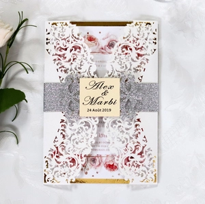 Detail of laser-cut floral wedding invitation with silver glitter band and custom tag