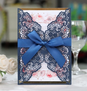 Detail of laser cut lace wedding invitation with navy blue sleeve and ribbon bow