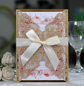 Detail of laser cut champagne gold wedding invitation with white satin bow and floral insert
