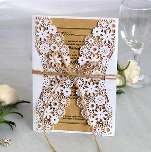 Detail of laser-cut white floral wedding invitation with kraft paper and rustic hemp bow