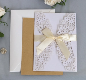Elegant laser cut floral wedding invitation suite with cream ribbon and kraft paper insert