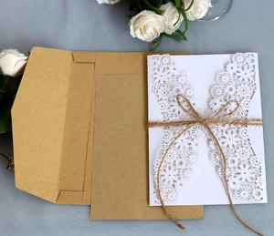 Detail of laser-cut white floral wedding invitation with kraft envelope and twine bow