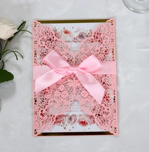 Detail view of pink laser-cut lace invitation with a silk ribbon bow and rose floral card
