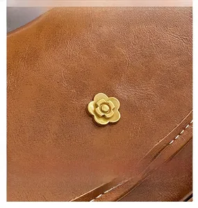 Close-up of caramel brown leather handbag with gold flower hardware and white stitching