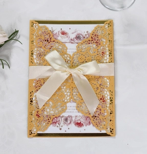 Detail of laser cut wedding invitation with golden floral lace and a cream silk ribbon bow