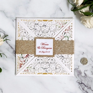 Detailed laser-cut white wedding invitation with a sparkling gold glitter belly band