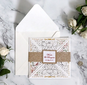 Detail of laser-cut wedding invitation with white floral sleeve and gold glitter belt