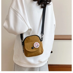 Détail d'un petit sac bandoulière en toile jaune moutarde avec écusson mignon et sangle