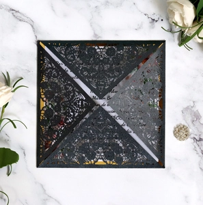 Macro view of black laser cut invitation card with lace floral details on marble surface