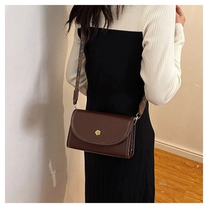 Detail of dark brown retro crossbody bag with golden flower hardware and jacquard strap