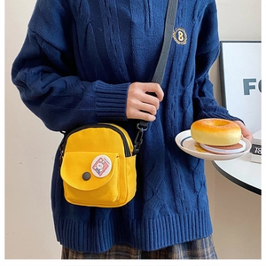 Détail du sac bandoulière en toile jaune avec badge cartoon et poche avant à rabat