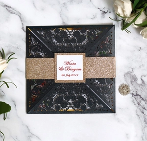 Macro shot of laser-cut floral patterns on black wedding invitation with gold glitter band