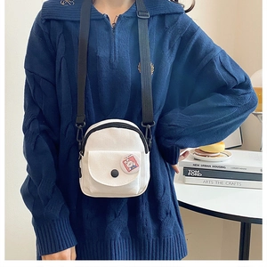 Détail d'un petit sac bandoulière en toile blanche avec broche et sangle noire réglable