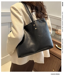Side view of a black faux leather tote bag worn by a model in a warm indoor setting