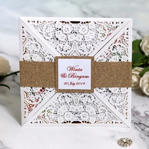 Laser cut white lace wedding invitation with a gold glitter belly band and marble background