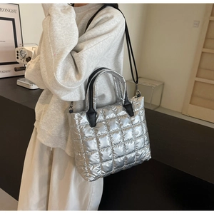Detail einer silbernen gesteppten Puffer-Tasche mit schwarzen Griffen und Metallglanz