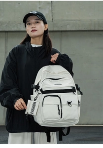 Detail of a beige multi-pocket backpack with black buckles and FASHION charm accessory