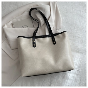 Detailed close-up of a white tote bag with black trim and gold hardware on a white blazer