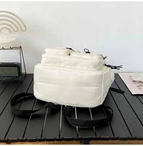Close-up of white utility backpack with multiple pockets on a minimalist background