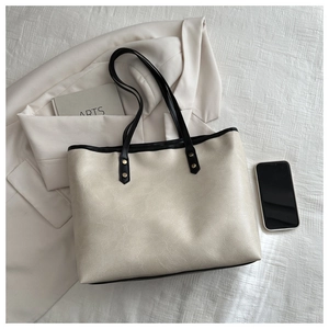 Detail of lychee textured beige tote bag with black trim and gold rivet accents