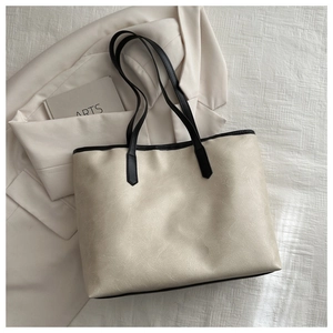 Detail of off-white leather tote bag featuring black contrast handles and premium texture