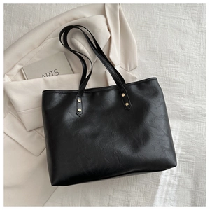 Close-up of black PU leather tote bag featuring gold rivet accents and dual shoulder straps