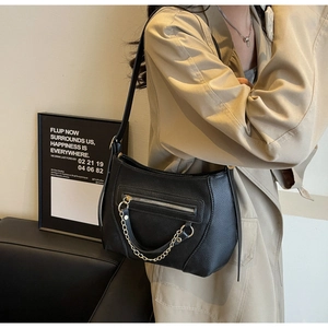 Detail of black pebbled leather tote bag with gold chain and front zipper pocket detail