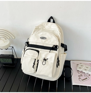 Detailed close-up of ivory nylon backpack featuring multi-pocket design and D-ring straps
