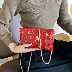Detail of red faux leather envelope bag with crocodile texture and gold chain strap