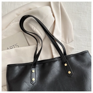 Close-up of black leather tote bag featuring golden rivets and premium textured finish