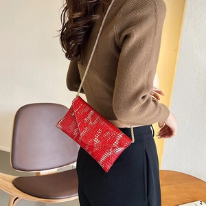 Detail of red crocodile pattern envelope chain bag with elegant golden strap on shoulder