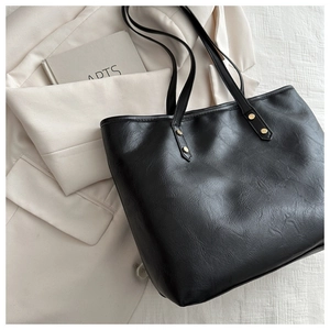 Detail of black faux leather tote bag showing fine texture and golden metal rivets