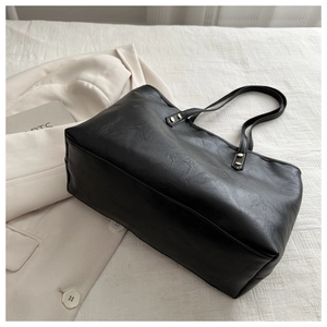 Detail of black tote bag with gold rivets and leather texture on a white fabric background