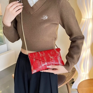 Detail of red crocodile textured leather clutch with elegant gold chain strap
