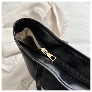 Close-up of golden zipper closure and beige lining on large black faux leather tote bag