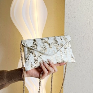 Close-up of white envelope chain bag featuring golden crocodile pattern texture