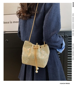 Detail of straw bucket bag featuring floral embroidery and elegant pearl accents