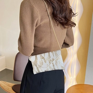 Detail view of a white envelope crossbody bag with gold animal texture and chain strap