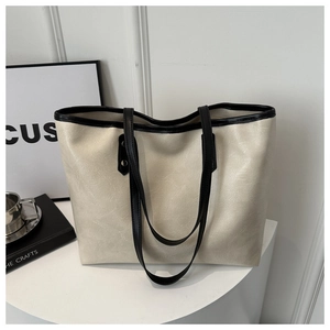 Detail view of large cream tote bag with black trim on a modern minimalist desktop