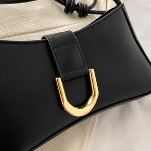 Detail of the golden D-shaped metal buckle on a black textured leather underarm handbag