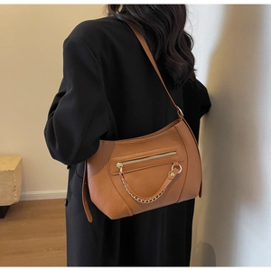 Detail view of brown pebbled leather shoulder bag with gold chain and front zip pocket