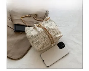 Detailed view of cream straw bucket bag with floral embroidery and size comparison with phone