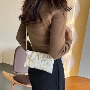 Detail showing white envelope bag with gold snake texture and slim chain strap