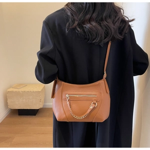 Detailed view of a brown leather tote bag featuring a gold chain on a black blazer