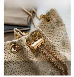 Detailed view of woven bucket bag with leaf embroidery and golden drawstring chain closure