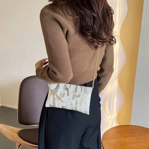 Detail of white envelope bag with golden animal print and metallic chain strap worn by model