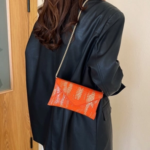 Detail of orange embossed leather envelope bag with gold chain strap on black leather jacket