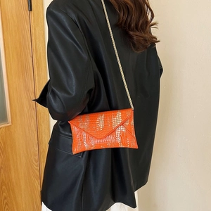 Detail of a vibrant orange envelope bag with animal pattern and thin gold chain strap
