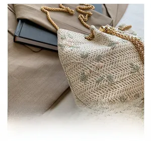 Detail of beige woven bucket bag featuring floral embroidery and gold metal chain strap