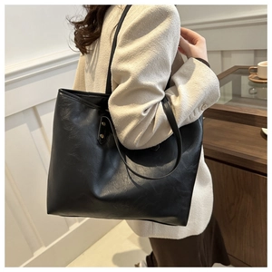 Detail of minimalist black tote bag with slim shoulder straps and gold rivet accents